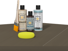 Retique It® Black Walnut kit with brush, Wood’n Primer, matte top coat, and yellow sponge on a wood surface.