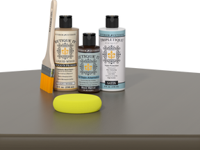 Retique It Black Walnut Kit with Satin Tripletique, Light Wood Wood'n Primer, Black Walnut Gel Stain Alternative, paintbrush, and yellow sponge on a tabletop.
