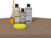 Retique It Barn Wood Kit with Light Wood Wood'n Primer, Barn Wood Gel Stain Alternative, Matte Polytique It topcoat, paintbrush, and yellow sponge on a tabletop.