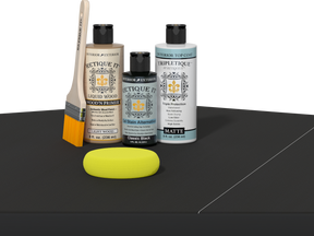 Retique It® Light Wood Wood’n Primer with Classic Black Gel Stain Alternative, matte topcoat, brush, and yellow sponge on a dark tabletop.