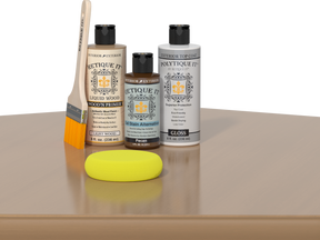 Retique It® Light Wood kit with brush, Pecan stain alternative, gloss top coat, and yellow sponge on a wood surface.