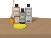 Retique It® Light Wood kit with brush, Pecan stain alternative, matte top coat, and yellow sponge on a wood surface.