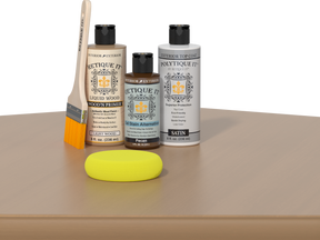 Retique It® Light Wood kit with brush, Pecan stain alternative, satin top coat, and yellow sponge on a wood surface.