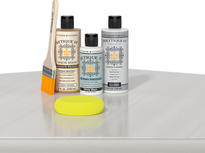 Retique It® Light Wood Wood’n Primer with White Wash Gel Stain Alternative, gloss topcoat, brush, and yellow sponge on a white tabletop.