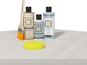 Retique It® Light Wood Wood’n Primer with White Wash Gel Stain Alternative, matte topcoat, and yellow sponge on a white tabletop.