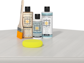 Retique It® Light Wood Wood’n Primer with White Wash Gel Stain Alternative, satin topcoat, brush, and yellow sponge on a white tabletop.