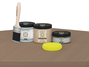 Painting supplies including a brush, jars of paint, and a sponge on a brown surface.