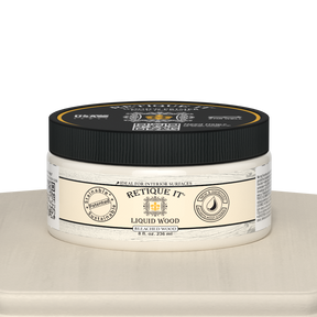 Retique It® Liquid Wood 8oz bleached interior paint jar on table, showing the clear glass container and white liquid inside.