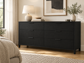 Ebony six-drawer dresser topped with a lamp, books, and greenery in a neutral bedroom.