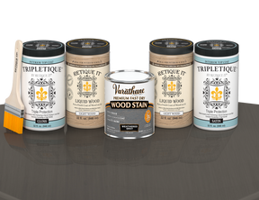 64 oz Retique It Liquid Wood kit with Weathered Gray stain, gloss Tripletique topcoat, and a paintbrush on a matching finished tabletop.
