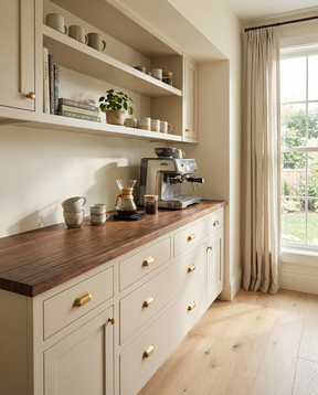 Kitchen with wooden countertop, white cabinets, and a window with curtains.